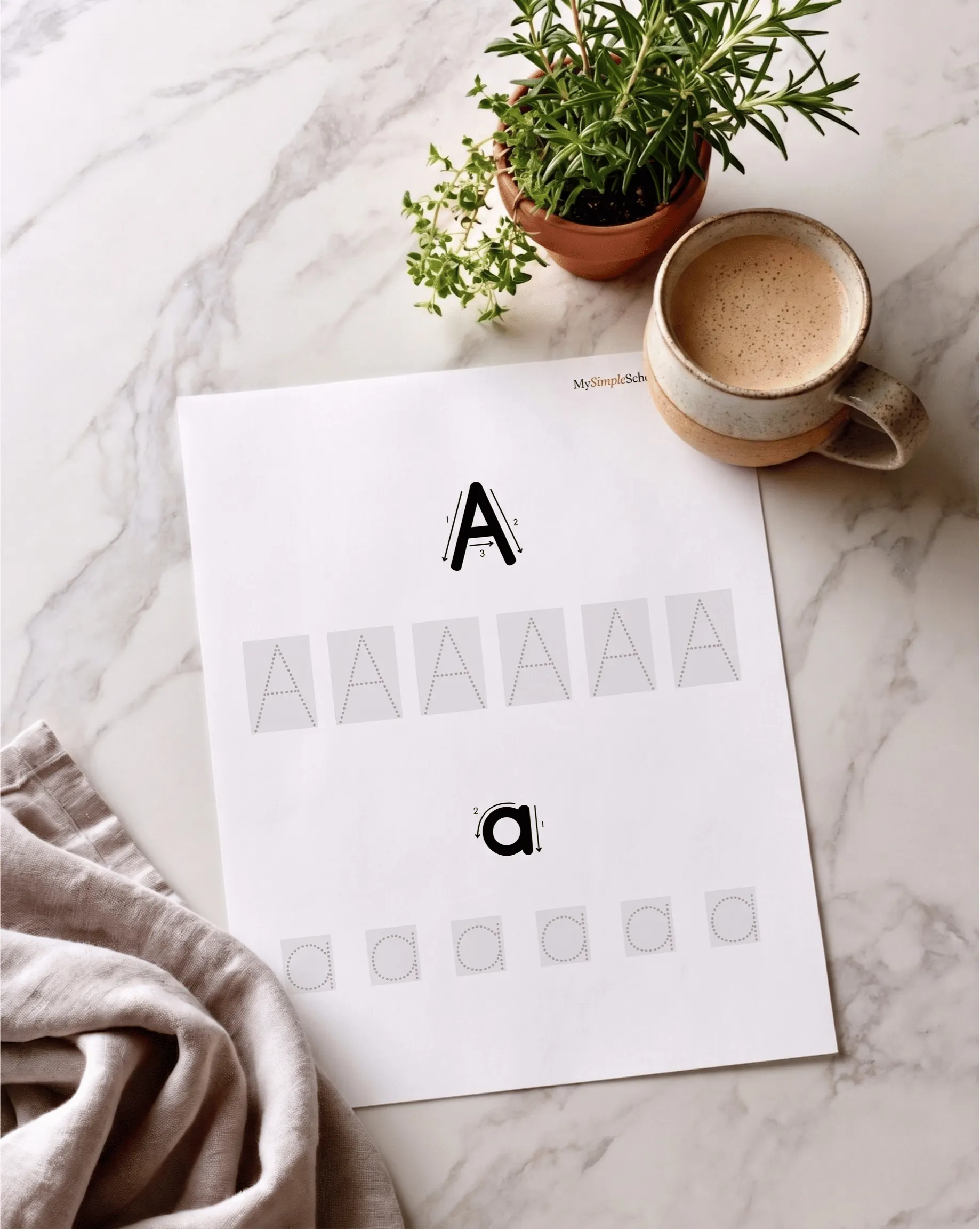 A printed My Simple Writing Sheets page for the letter A on a marble counter, beside a cup of coffee.