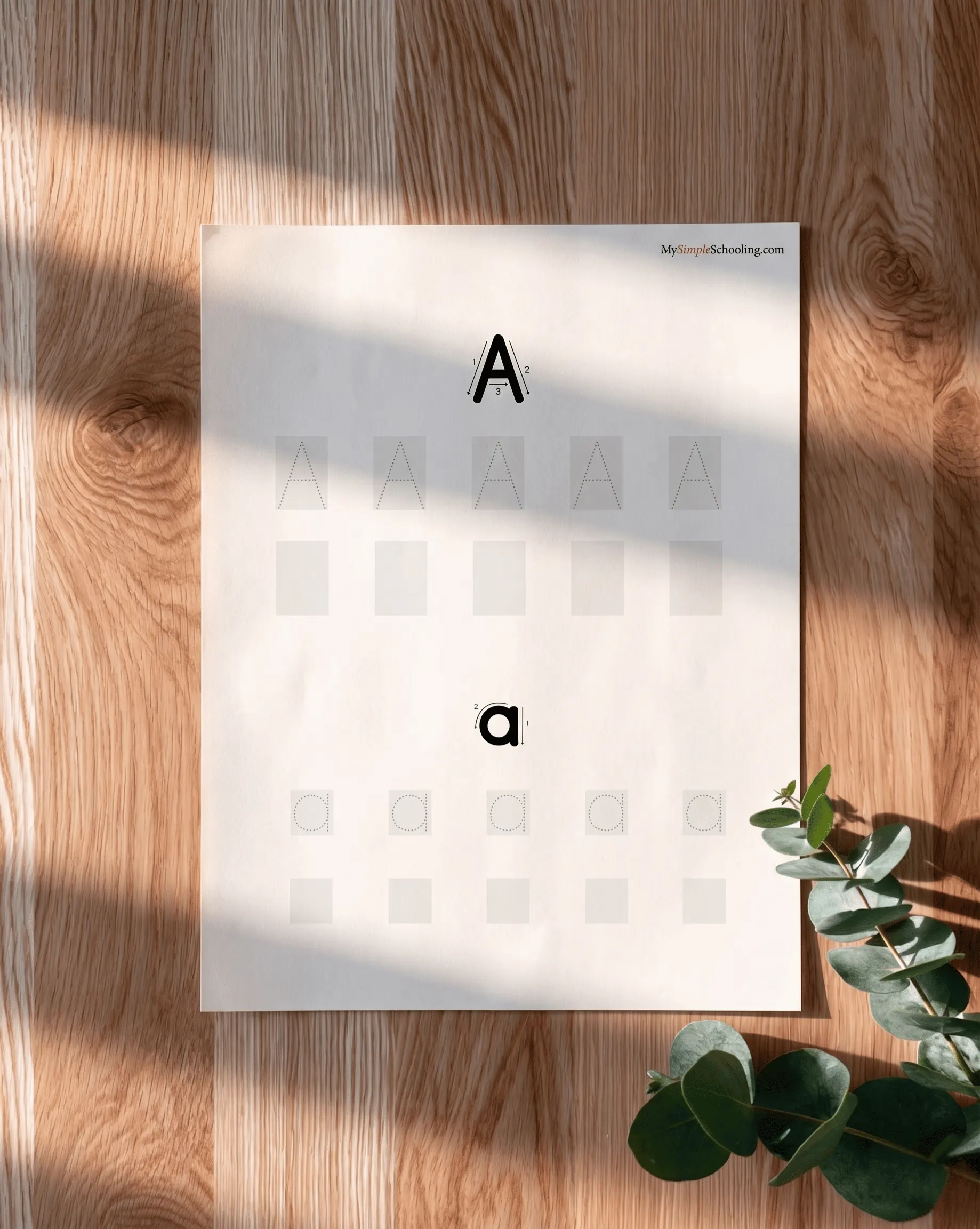A My Simple Writing Sheets letter page on an oak table with eucalyptus, in soft daylight.