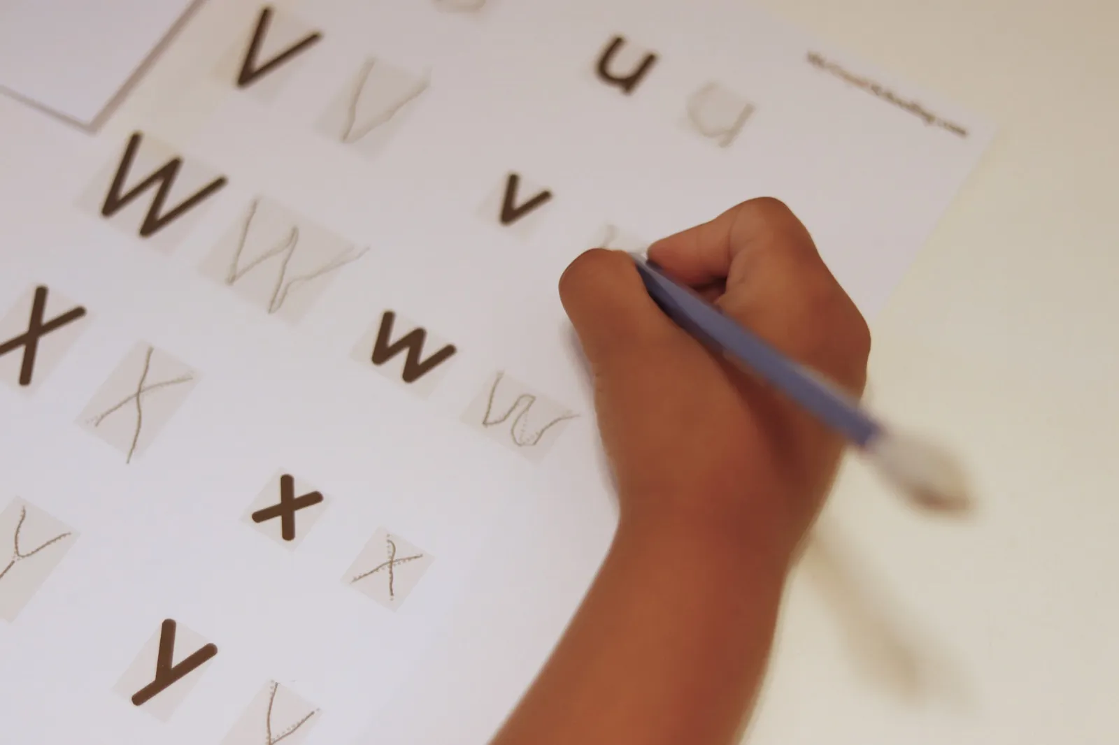 A child filling in a Level 1 Alphabet Overview sheet, tracing the letters by hand.