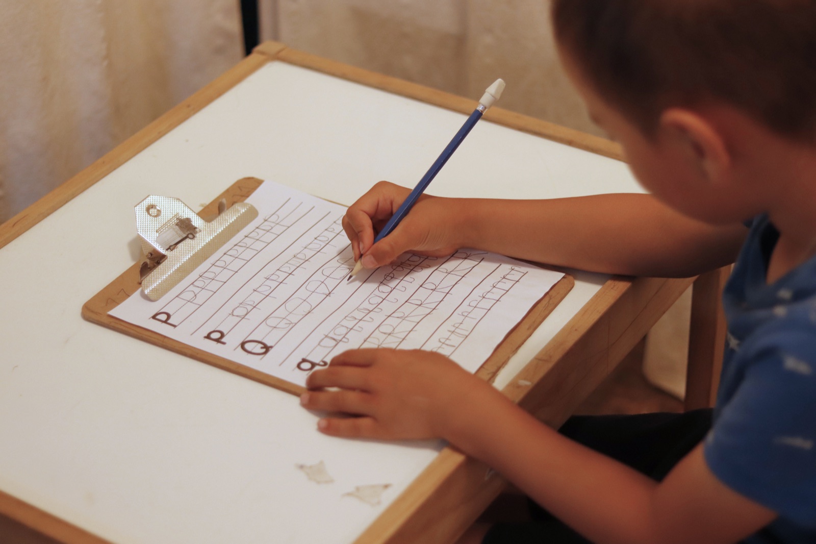A child from the My Simple Schooling family writing on a practice sheet at home